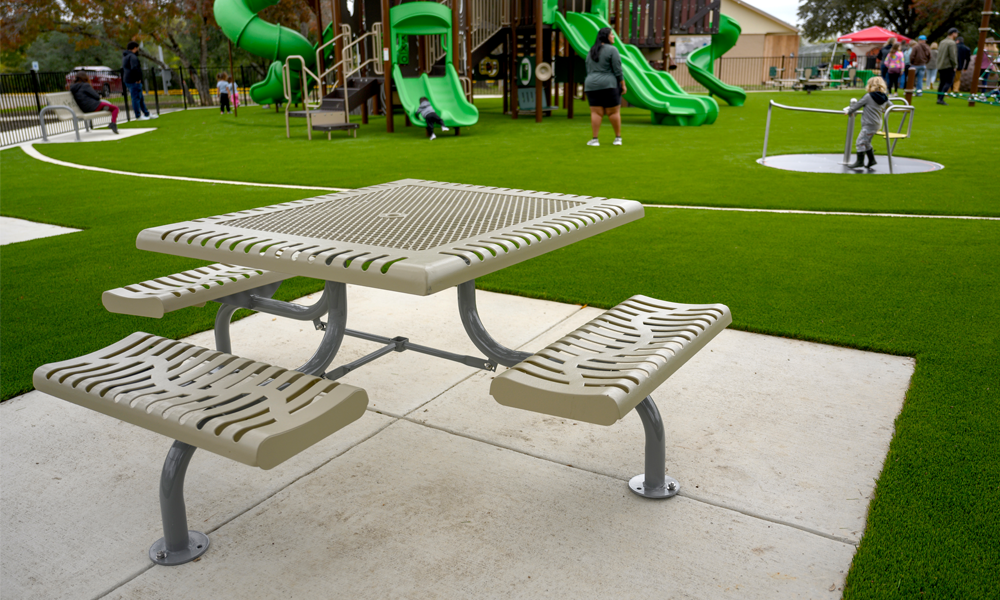 Commercial thermoplastic square picnic table with surface mount frame installed beside a playground and artificial turf recreation area